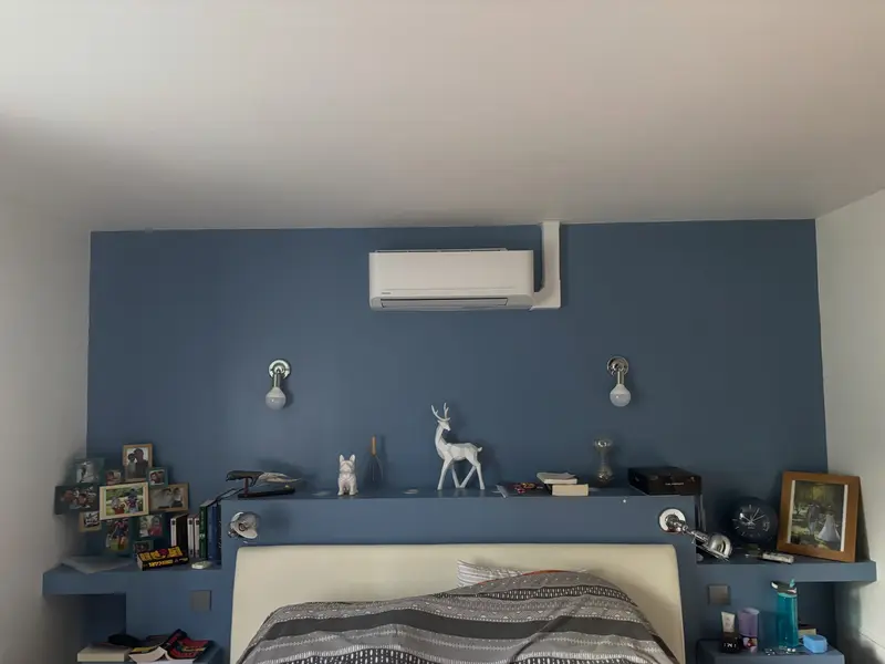 Climatisation murale posée au-dessus d'un lit, mur bleu